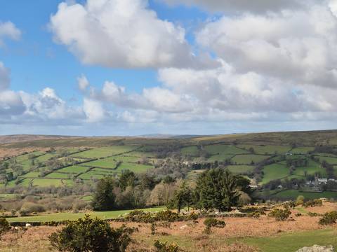       Expansive view of rolling green moorland and patchwork fields beneath a partly cloudy sky.
  