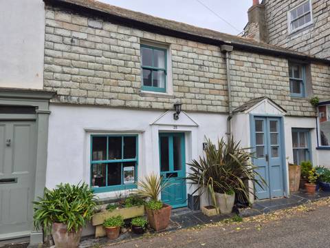       Charming white-washed cottage with teal doors and windows adorned by potted plants.
  