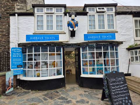       Quaint seaside shop ‘Harbour Treats’ with blue signage and colourful window displays in Port Isaac.
  