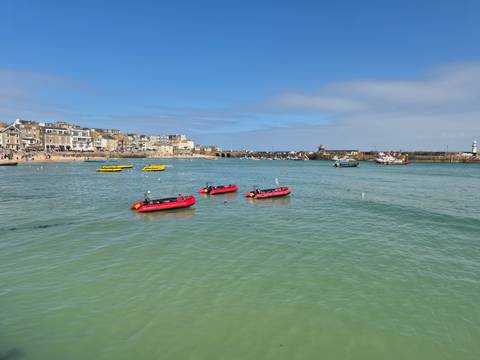       Clear turquoise harbour with red inflatable boats floating near the quays of St Ives.
  