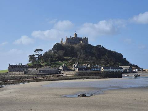       Medieval castle atop St Michael’s Mount rising above a small Cornish village at low tide.
  
