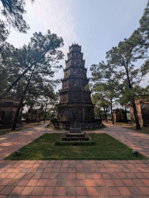       Ancient octagonal brick Thien Mu Pagoda tower framed by tall pines in Hue
  