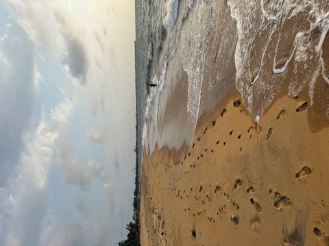       Footprint-studded sandy beach with gentle waves under a partly cloudy sky.
  