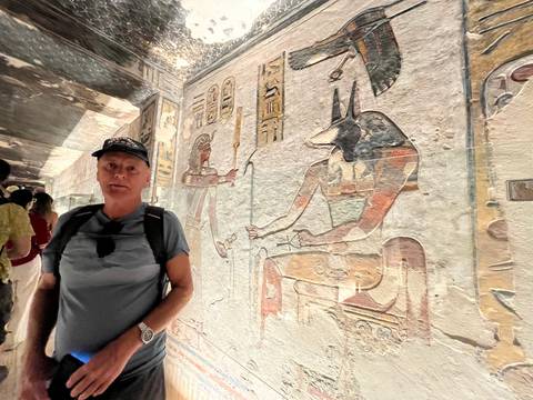       Visitor stands beside vividly painted reliefs of Egyptian gods inside a tomb
  