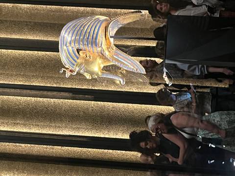       Golden funerary mask displayed in a museum with visitors gathered around
  