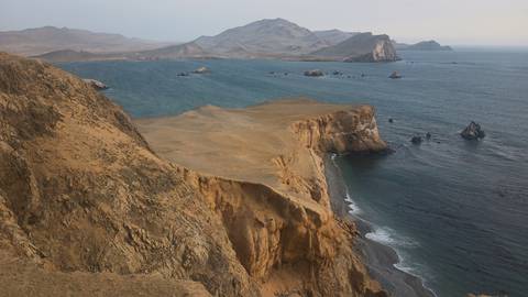       Wide coastal panorama of rugged tan headlands meeting deep blue ocean with scattered rock stacks.
  
