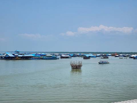       Floating village of blue-roofed houses spread across a vast lake on a clear day.
  