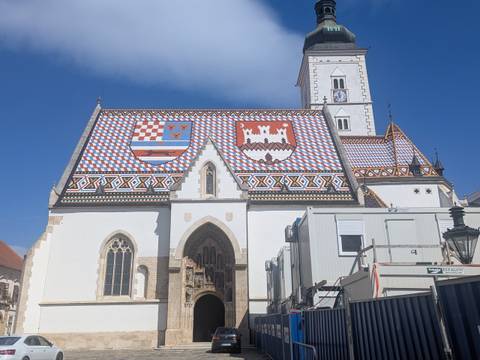       St. Mark’s Church with its vividly patterned tiled roof under a bright blue sky.
  