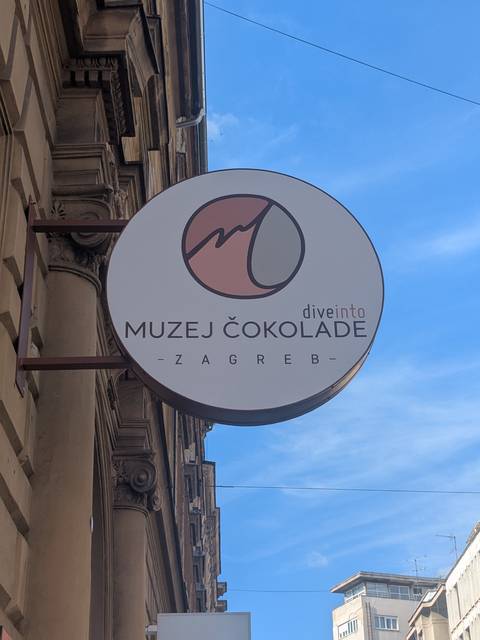       Round sign for the Zagreb Chocolate Museum hanging on a city building facade.
  