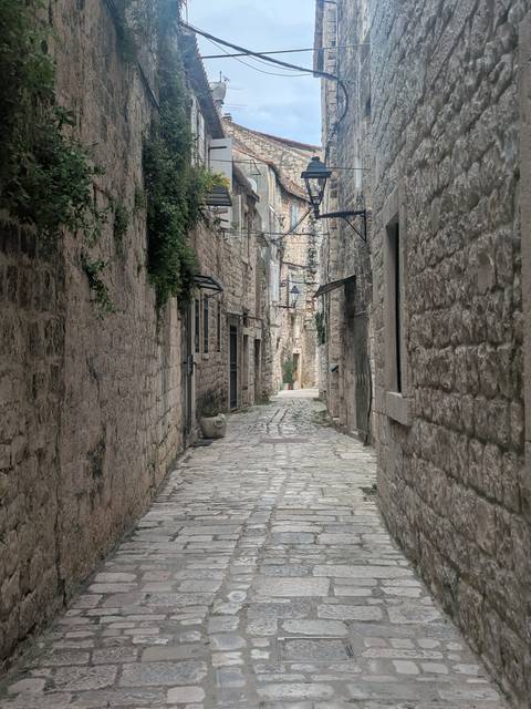       Quiet narrow stone alleyway with rustic walls and hanging lanterns.
  