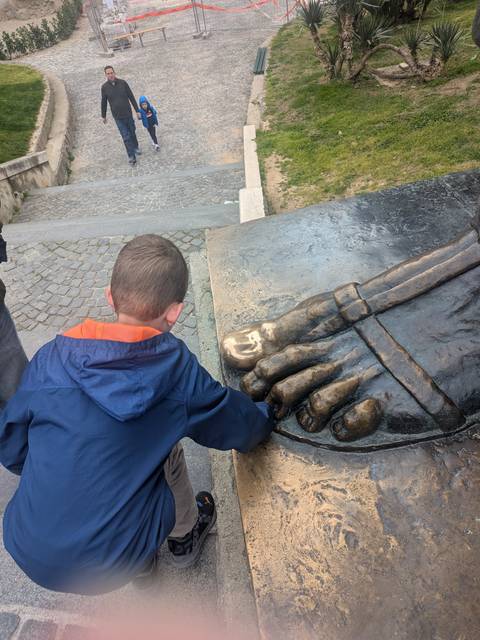       Child polishing the bronze toe of a large historic statue for good luck.
  