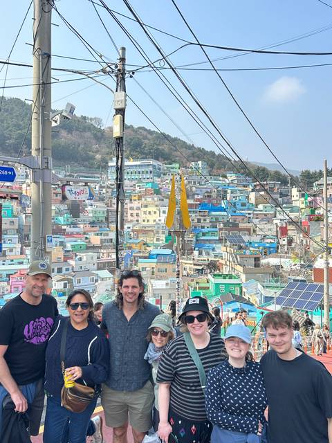       Visitors stand before the colourful stacked houses of Gamcheon Culture Village.
  