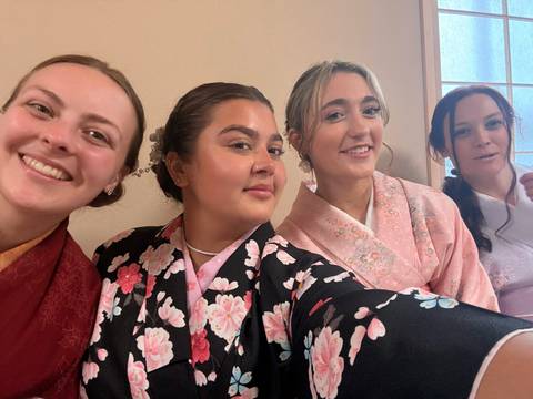       Four young women in colorful kimonos smiling for a close-up selfie indoors.
  