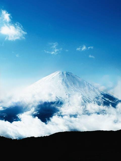      Snow-covered Mount Fuji emerging above a sea of clouds under a brilliant blue sky.
  
