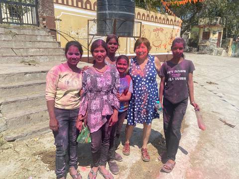       Women joyfully covered in vibrant Holi powders pose together in an Indian village street
  