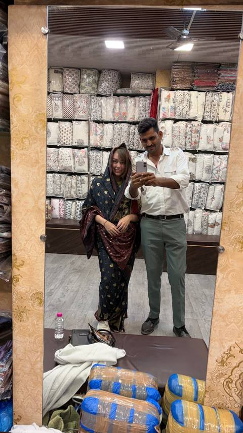       Tourist and local guide take a mirror selfie inside a textile shop
  