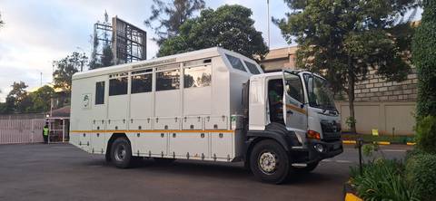       Large white overland safari truck parked outside a city compound, ready for an expedition
  