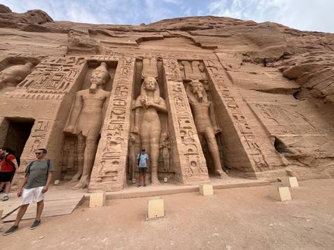       Rock-cut façade of Abu Simbel’s smaller temple with hieroglyphics; a tourist stands between carved figures.
  