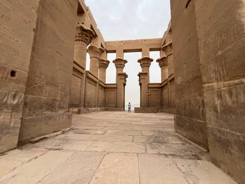       Tall papyrus-style columns frame a lone person standing in the courtyard of Philae Temple.
  