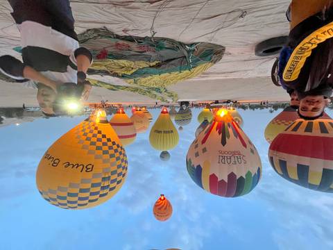       Multiple colorful hot-air balloons inflation on a launch field at dawn with excited passengers.
  