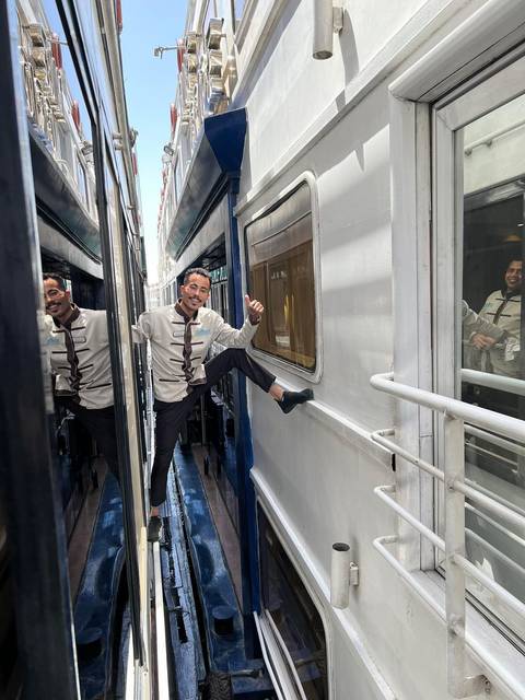       A cheerful train attendant poses between two carriages of a Nile cruise train.
  
