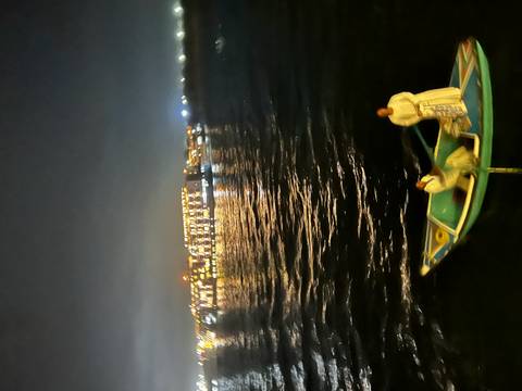       Blurry nighttime shot of two men in a small boat on the Nile with city lights behind.
  