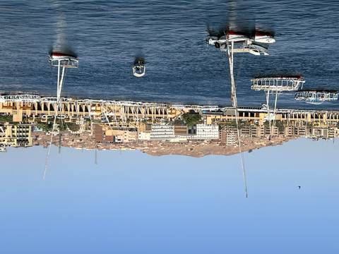       Daytime view over the Nile with sailboats moored opposite a hillside cityscape in Aswan.
  