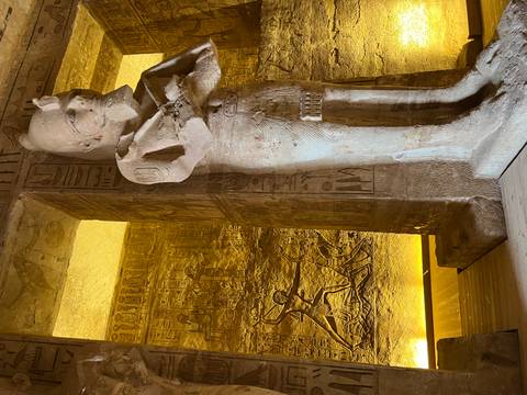       Interior statue of Ramses with illuminated hieroglyph walls inside an Egyptian temple.
  