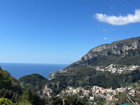      Wide coastal landscape of the Amalfi Coast with hillside villages and deep blue sea under a clear sky.
  