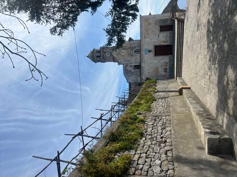       Stone church with clock tower in a small Italian hill town beneath streaked clouds.
  
