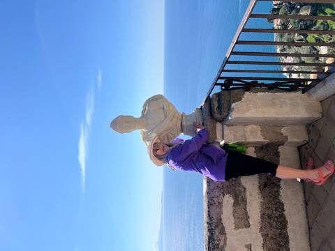       Woman playfully posing with a marble bust on a seaside terrace high above the Amalfi Coast.
  