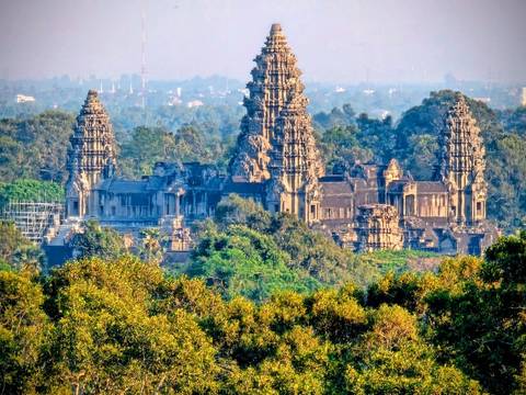       Elevated telephoto view of majestic Angkor Wat temple towers rising above dense jungle.
  