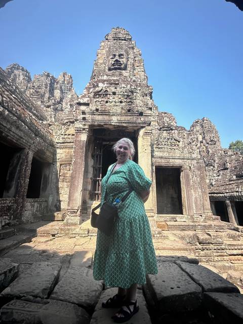       Traveler posing in front of intricately carved stone doorway at an Angkor temple.
  