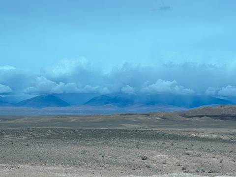       Wide arid plain with distant mountains beneath a bank of dramatic clouds.
  