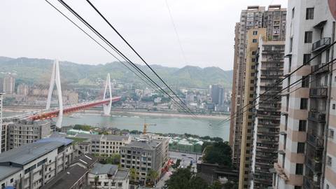       Daytime cityscape of Chongqing featuring a red-white cable-stayed bridge spanning the Yangtze River framed by apartment blocks.
  