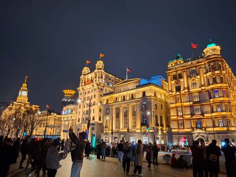       The Bund in Shanghai lit golden at night with crowds of visitors along the promenade and iconic historic buildings.
  