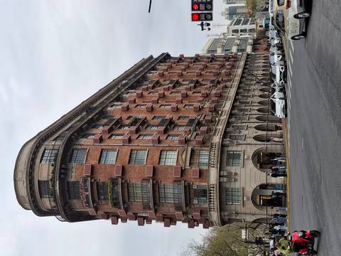       Historic red-brick Normandie apartment building (Wukang Mansion) on a gray day with traffic and pedestrians below.
  