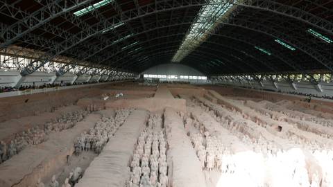       Wide interior shot of the main pit of the Terracotta Army in Xi’an, rows of clay warriors under a vast arched hangar roof with visitors along the sides.
  