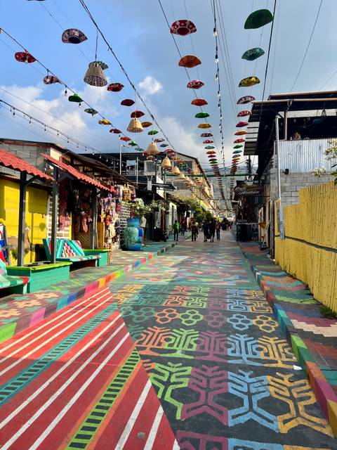       Vibrant pedestrian street with multicoloured painted pavement, hanging umbrellas and handicraft shops in a Guatemalan lakeside town.
  