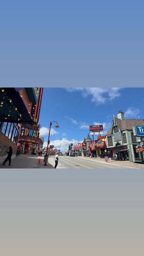       Colourful Clifton Hill entertainment strip in Niagara Falls lined with neon signs and themed attractions on a bright day.
  