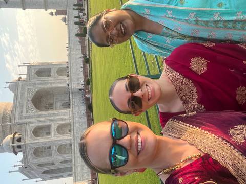      Selfie of three women in colorful saris with the marble Taj Mahal grandly rising behind.
  