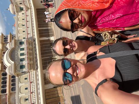       Three travelers smiling in front of ornate Jaipur City Palace courtyard on a sunny day.
  