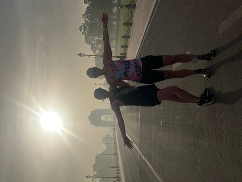       Silhouetted pair posing playfully on an empty boulevard at sunrise with India Gate in hazy distance.
  