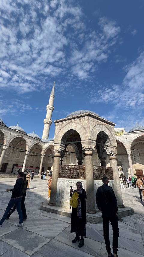       Courtyard of the Blue Mosque with elegant marble arches and minaret reaching into a partly cloudy sky.
  
