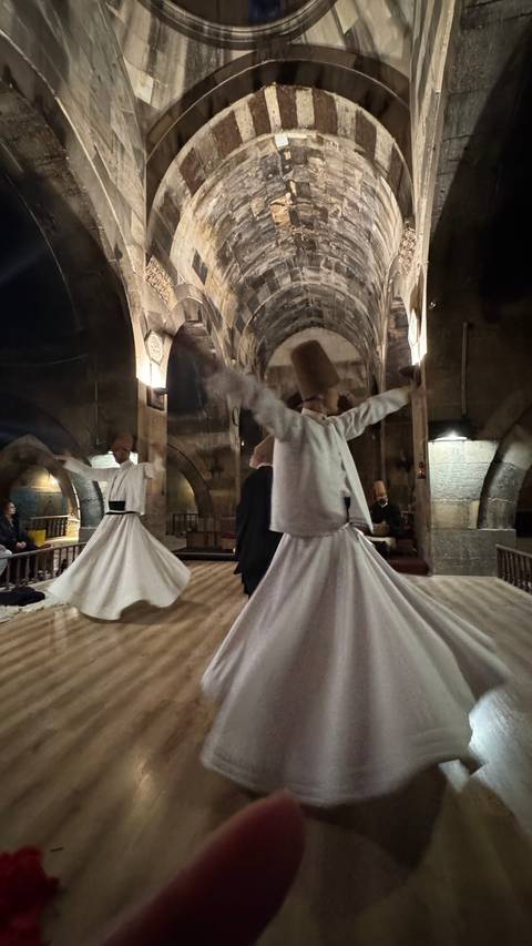       Blurred low-light image of whirling dervish ceremony inside historic stone hall.
  