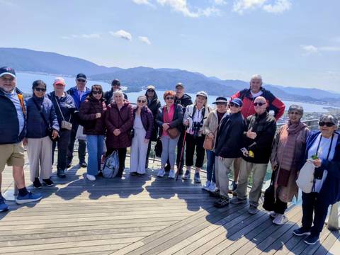       Tour group posing on wooden viewing deck overlooking bay and mountains in Japan
  