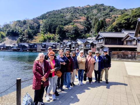       Tourists standing beside traditional waterside boathouses in coastal Japanese village
  
