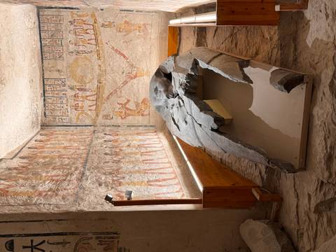       Fragmented granite sarcophagus inside vividly painted Egyptian tomb chamber
  
