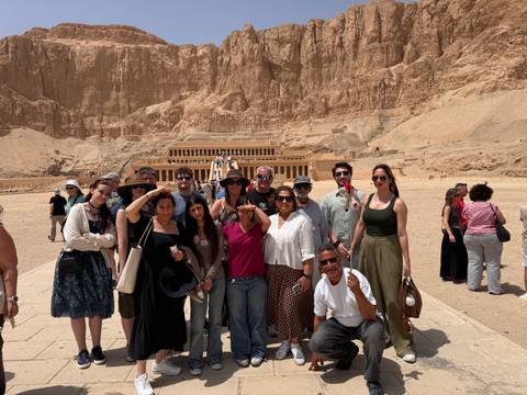       Tour group posing in front of Hatshepsut Temple against towering cliffs
  