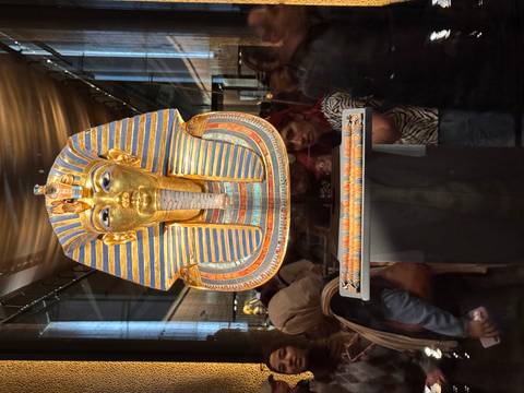       Golden funerary mask of Tutankhamun displayed in Cairo museum with crowd
  